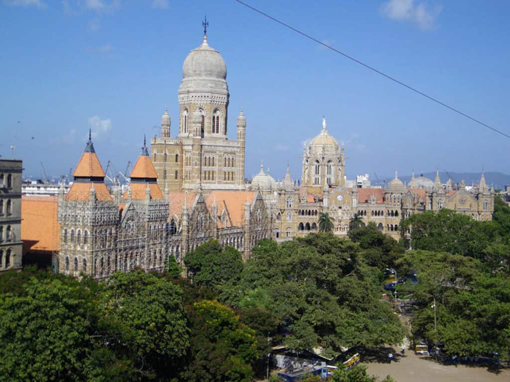 A view of the gothic BMC (Municipal Body) Headquarters on the left with the historic Mumbai CST station in the background on the right on a clear, blue sky day.