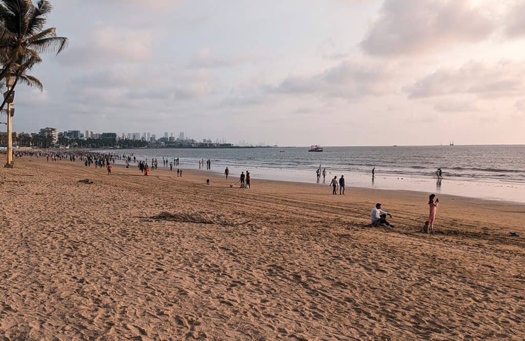 A sunset at a busy sandy beach in Western Mumbai. It is the early evening and you can see yellow hues in the sky with sparse clouds. 