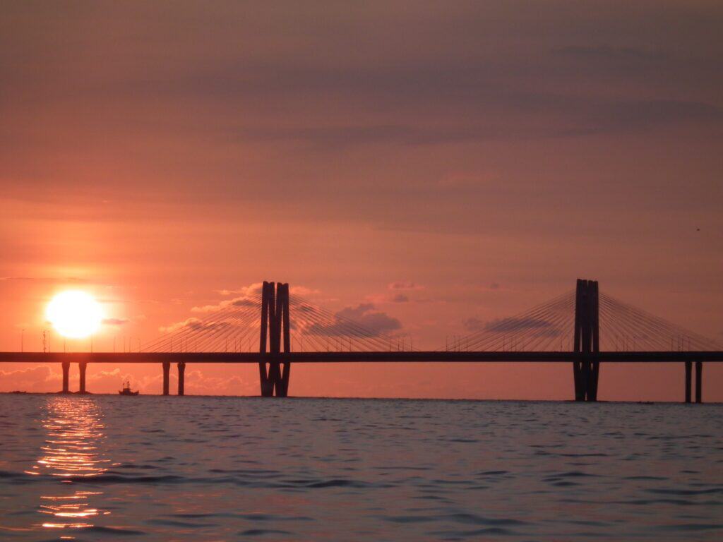 A view of the Banra-Worli sea bridge in Mumbai at sunset. The sun is just behind the bridge and there is an orange glow in the sky. 