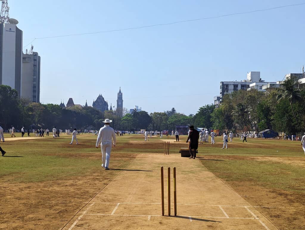 A cricet pitch at the Cross Maidan or ground in Mumbai. You can also see other cricket pitches in the same shot with old and new buildings of Mumbai in the background.  