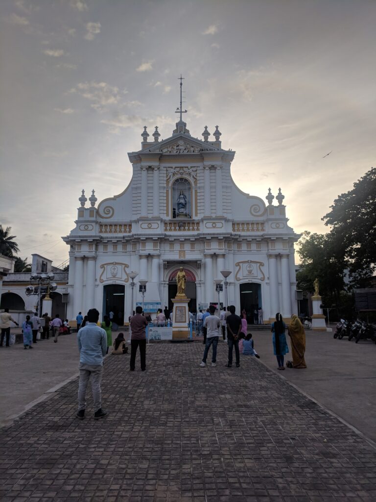 A picture of a medieval church at sunset in Pondicherry, India. The church is a silhouette against the setting sun. The church is white in color. 