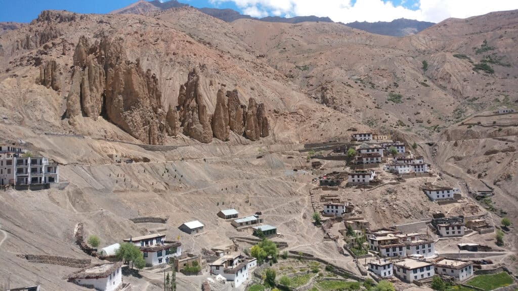 A rugged mountainous landscape with red, rocky mountains of Spiti valley in India. There is a little village with white houses along the mountainside.