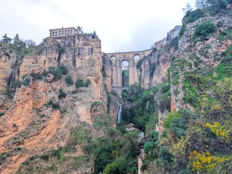 A view of the Puente Nuevo bridge in Ronda, Spain. The picture is taken from the bottom of the canyon looking up at the three arched medieval bridge. Buildings of the town of Ronda can be seen on either sides of the bridge.