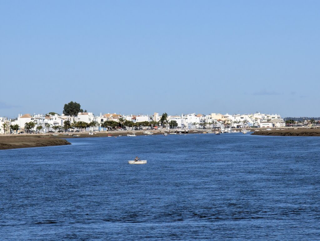 A picture of a lagoon in Algarve, Portugal. The lagoon has a single boat on blue waters with a white town in the background.