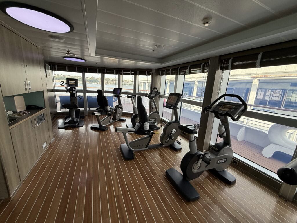 Fitness center aboard Ponant’s L’Austral, with stationary bikes, cardio equipment and large windows overlooking the ship’s deck and harbor.