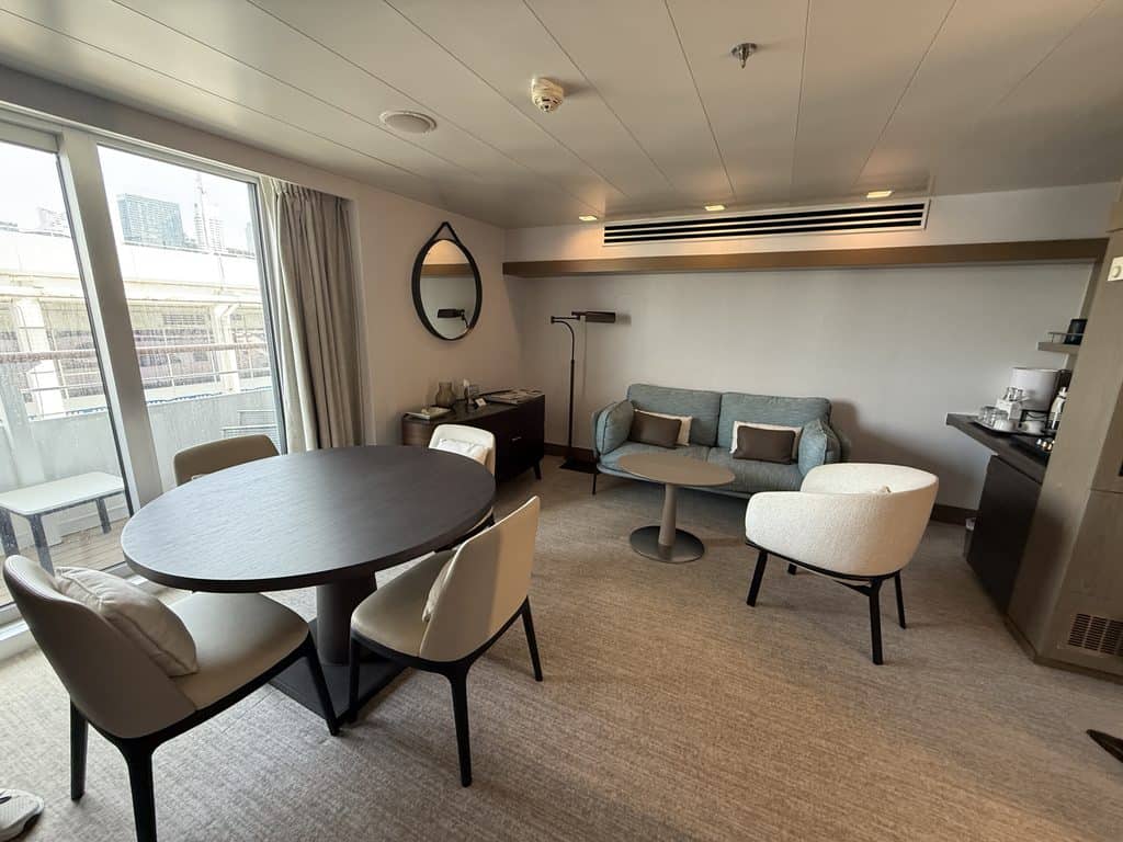 Suite living area aboard Ponant’s L’Austral, with a dining table for four, blue sofa, armchair and sliding glass doors to a furnished balcony.