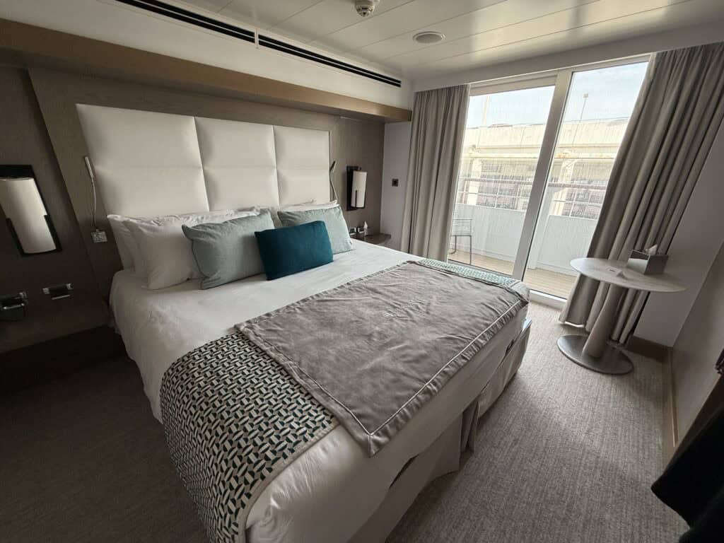 Balcony stateroom aboard Ponant’s L’Austral, featuring a double bed, teal accent pillows and sliding glass doors opening onto a private balcony.